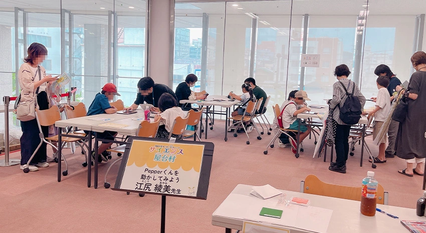 プログラミングに取り組む小学生と見守る保護者の皆さん、サポーターの理工系の学生たち